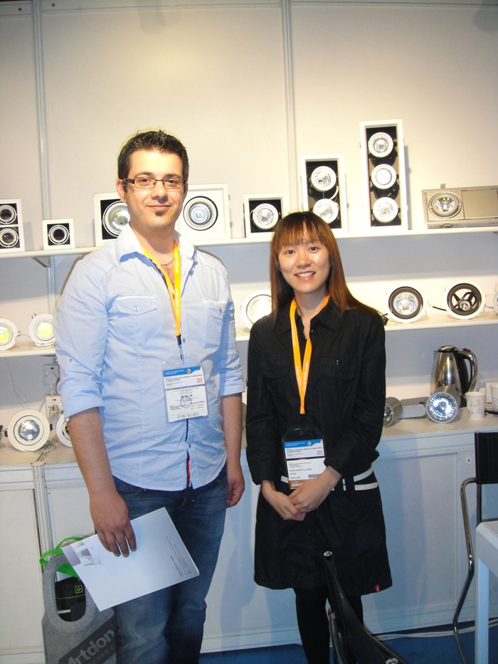 Two people standing beside the luminaire display shelves.